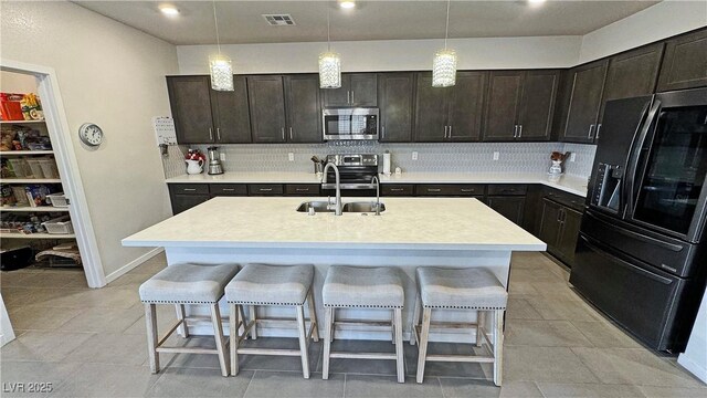 kitchen with light countertops, stainless steel appliances, a sink, a breakfast bar area, and backsplash