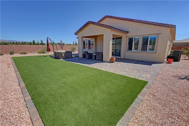 rear view of property featuring stucco siding, a hot tub, a patio, a fenced backyard, and a lawn