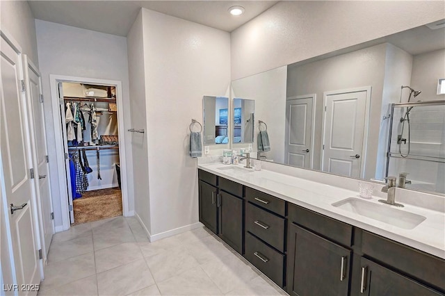 bathroom featuring double vanity, a sink, a stall shower, and a walk in closet