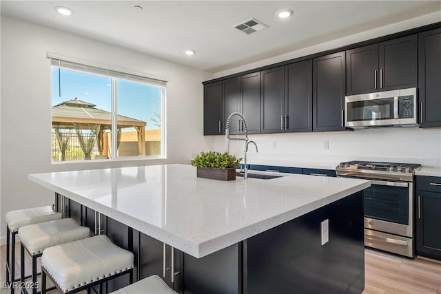 kitchen with visible vents, an island with sink, appliances with stainless steel finishes, light stone countertops, and recessed lighting