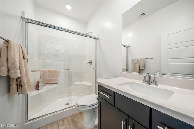 full bath featuring toilet, wood finished floors, vanity, visible vents, and a stall shower