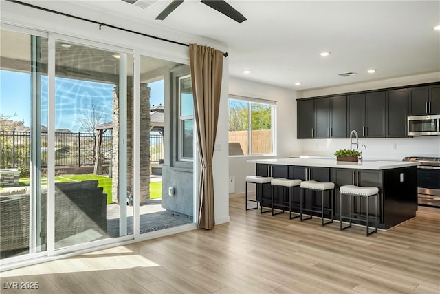 kitchen with a kitchen breakfast bar, light countertops, appliances with stainless steel finishes, light wood finished floors, and an island with sink