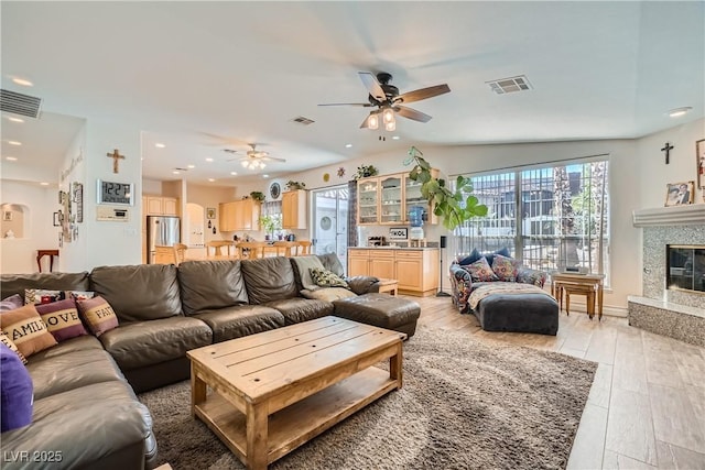 living area featuring light wood-type flooring, a glass covered fireplace, and visible vents