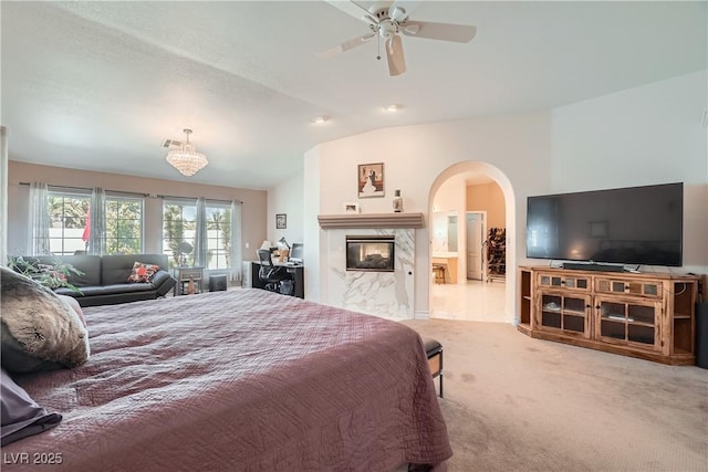 carpeted bedroom with visible vents, arched walkways, lofted ceiling, ensuite bath, and a premium fireplace