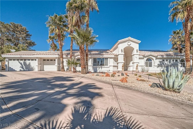 mediterranean / spanish house featuring a garage, solar panels, a tile roof, concrete driveway, and stucco siding