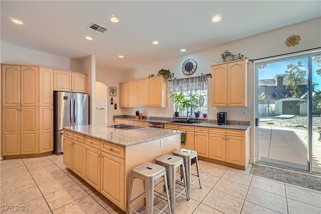 kitchen featuring visible vents, arched walkways, a kitchen island, freestanding refrigerator, and light brown cabinets