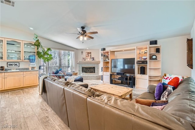 living area with visible vents, light wood-style flooring, a ceiling fan, a high end fireplace, and vaulted ceiling