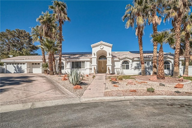 mediterranean / spanish house with a garage, a tile roof, driveway, roof mounted solar panels, and stucco siding