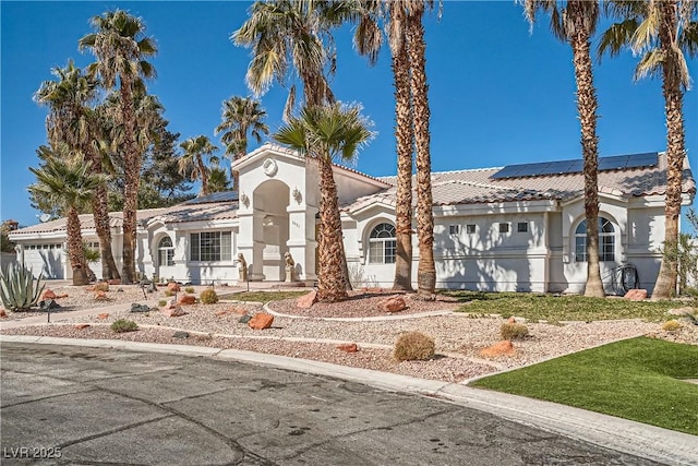 mediterranean / spanish-style house featuring solar panels, a tiled roof, an attached garage, and stucco siding