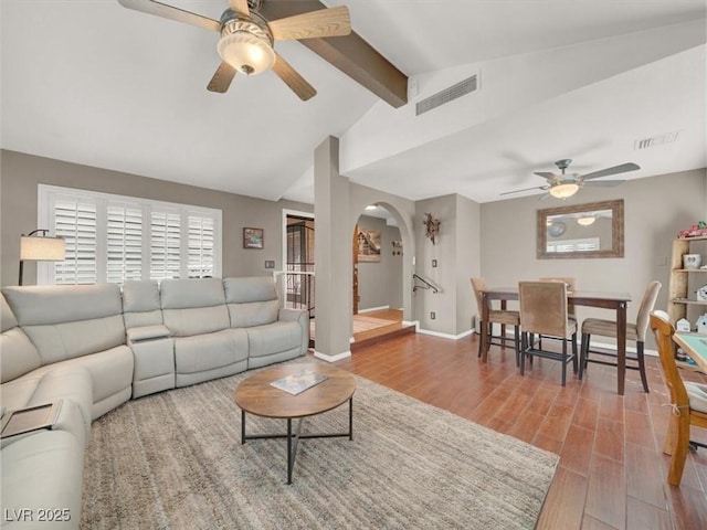 living area featuring arched walkways, visible vents, vaulted ceiling with beams, and wood finished floors