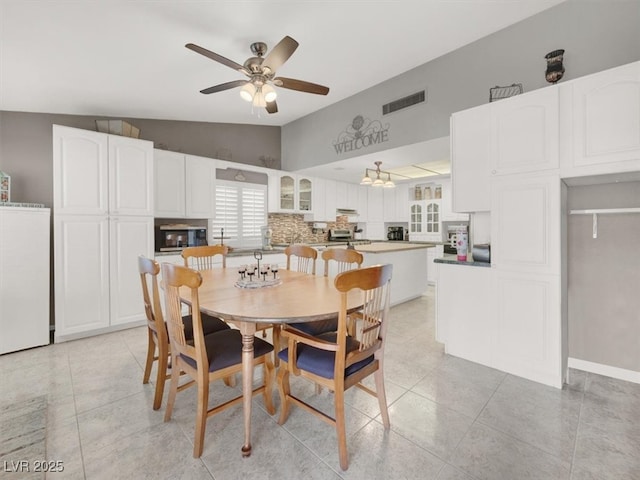 dining space with light tile patterned floors, visible vents, vaulted ceiling, and a ceiling fan