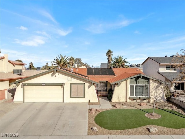 view of front of home with a garage, central AC unit, concrete driveway, roof mounted solar panels, and stucco siding