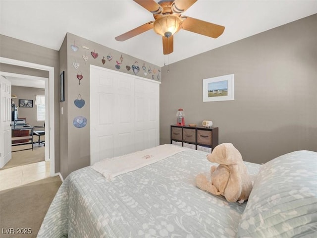 bedroom with a closet, light colored carpet, a ceiling fan, light tile patterned flooring, and baseboards