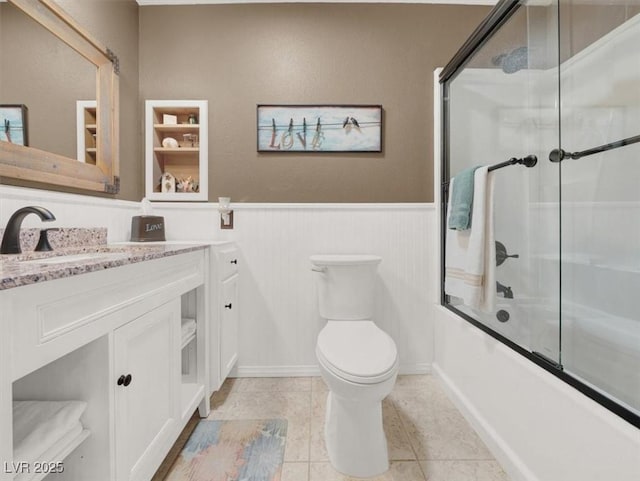 full bathroom featuring bath / shower combo with glass door, wainscoting, toilet, tile patterned floors, and vanity