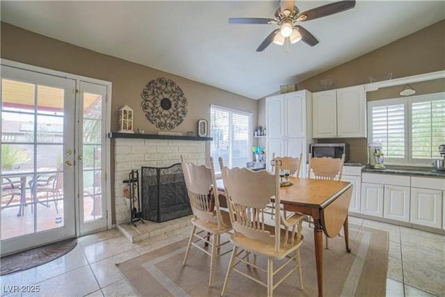 dining room featuring a fireplace, vaulted ceiling, a ceiling fan, and light tile patterned flooring