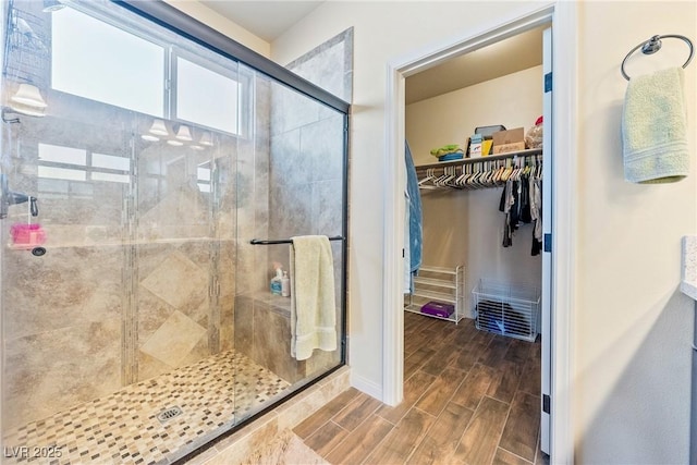 full bath featuring baseboards, a spacious closet, a stall shower, and wood tiled floor