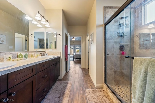 bathroom with a stall shower, connected bathroom, a ceiling fan, wood finish floors, and a sink