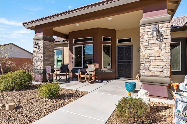 entrance to property with covered porch, stone siding, a tiled roof, and stucco siding