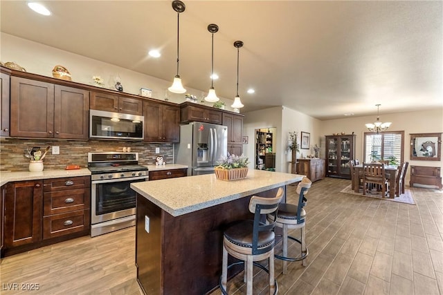 kitchen featuring dark brown cabinetry, stainless steel appliances, decorative backsplash, a center island, and light wood finished floors