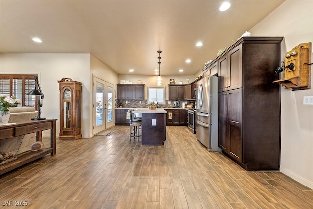 kitchen with dark brown cabinetry, light wood finished floors, appliances with stainless steel finishes, a breakfast bar, and french doors