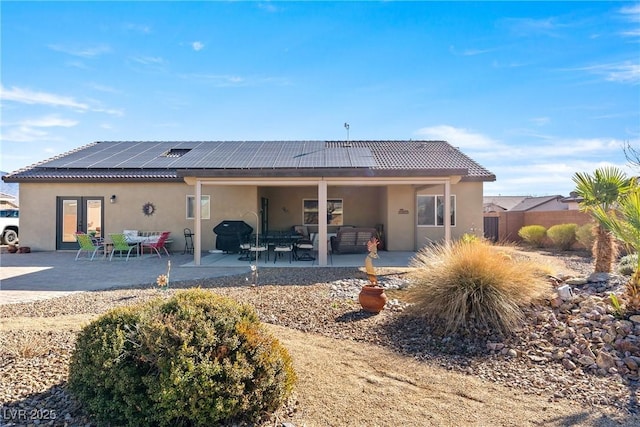 back of property with fence, french doors, a patio area, roof mounted solar panels, and stucco siding