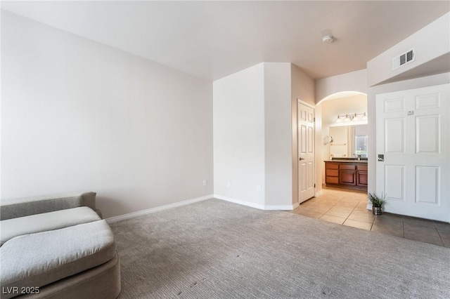 living area featuring arched walkways, light tile patterned floors, light colored carpet, visible vents, and baseboards