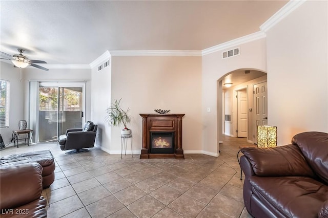 tiled living room featuring arched walkways, visible vents, baseboards, ornamental molding, and a glass covered fireplace