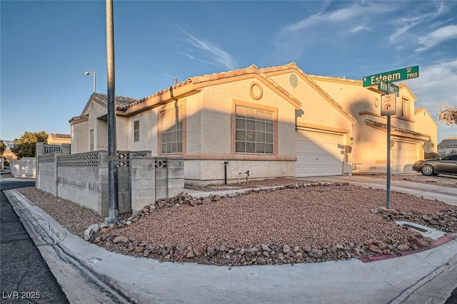 view of front of home with a fenced front yard, an attached garage, driveway, a tiled roof, and stucco siding