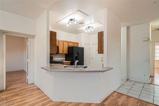 kitchen with light countertops, brown cabinetry, a sink, light wood-type flooring, and black appliances