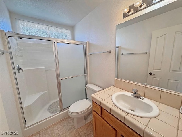 bathroom with a textured ceiling, tile patterned flooring, toilet, vanity, and a stall shower
