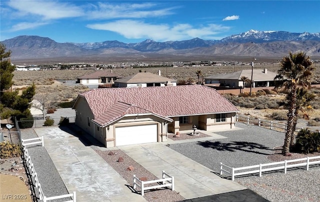 view of front facade with concrete driveway, a fenced front yard, a tiled roof, a mountain view, and stucco siding