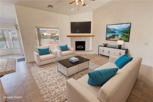 living area with lofted ceiling, ceiling fan, visible vents, tile patterned floors, and a tiled fireplace