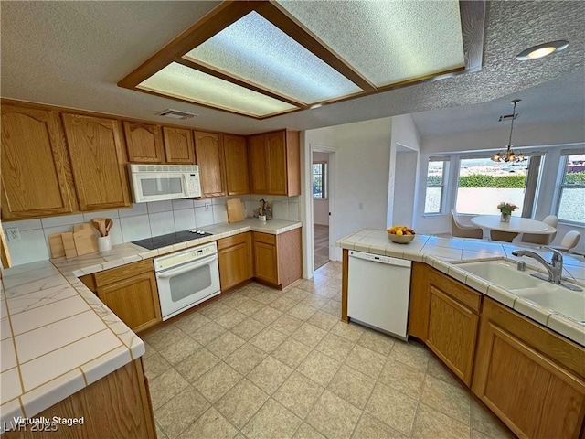 kitchen featuring light floors, tile counters, visible vents, brown cabinetry, and white appliances