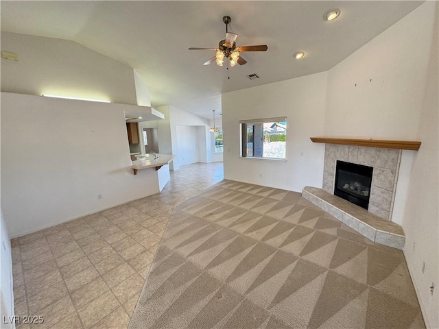 unfurnished living room featuring a tile fireplace, visible vents, vaulted ceiling, and ceiling fan