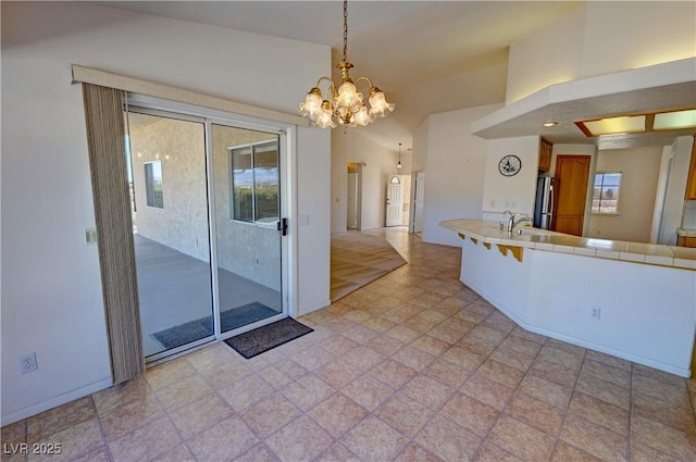 kitchen with tile counters, brown cabinets, freestanding refrigerator, a healthy amount of sunlight, and a sink