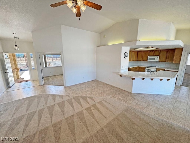 kitchen with lofted ceiling, white microwave, brown cabinets, a peninsula, and light countertops