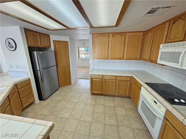 kitchen with tasteful backsplash, white appliances, visible vents, and tile countertops