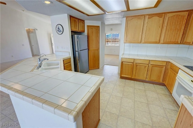 kitchen featuring tile counters, oven, a sink, freestanding refrigerator, and backsplash