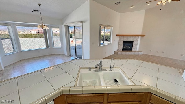 kitchen with visible vents, tile countertops, open floor plan, vaulted ceiling, and a sink
