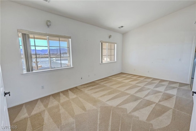 empty room featuring lofted ceiling, visible vents, a wealth of natural light, and light colored carpet