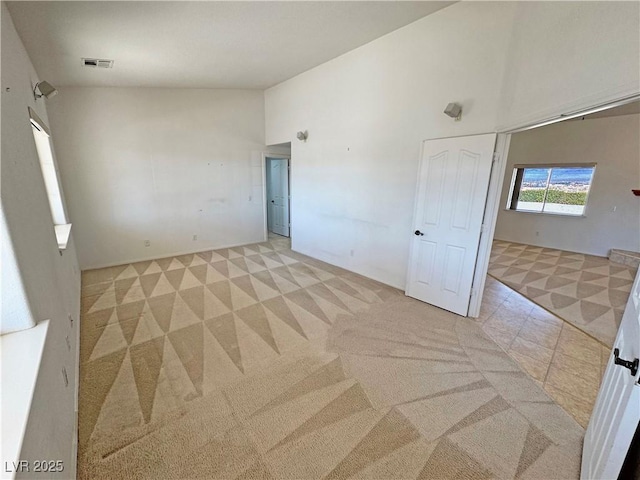 unfurnished bedroom featuring high vaulted ceiling, visible vents, and light colored carpet
