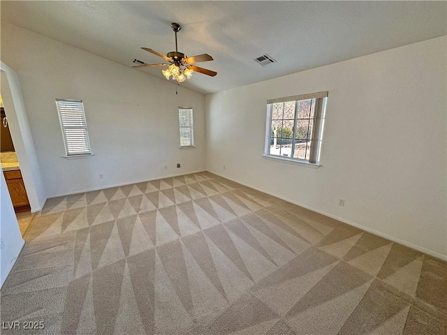 spare room featuring ceiling fan, light colored carpet, visible vents, baseboards, and vaulted ceiling