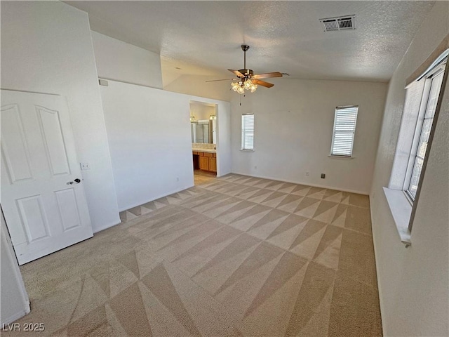 spare room featuring visible vents, light carpet, vaulted ceiling, a textured ceiling, and baseboards