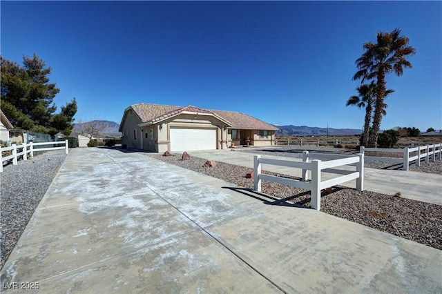 view of side of property featuring a fenced front yard, concrete driveway, a mountain view, and an attached garage