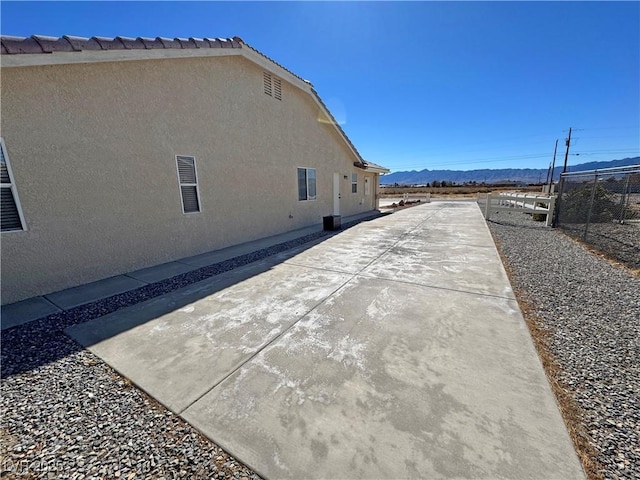 view of side of property with a patio area, fence, a mountain view, and stucco siding