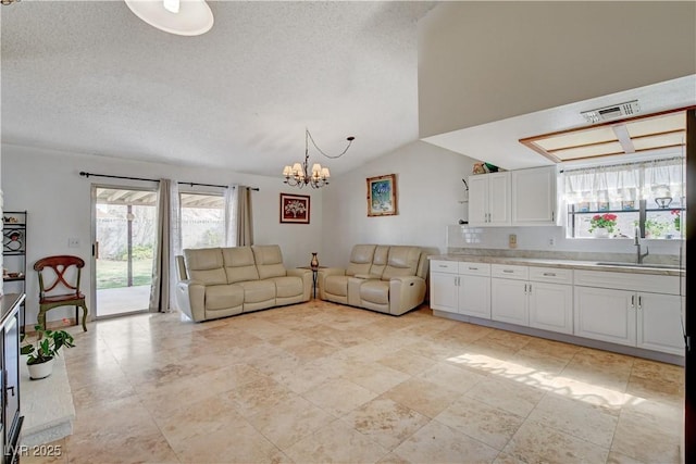 unfurnished living room featuring visible vents, vaulted ceiling, a textured ceiling, a chandelier, and a sink