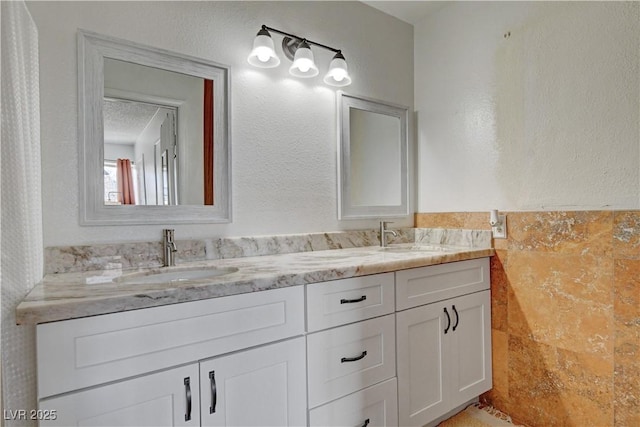 bathroom with a textured wall, a sink, and double vanity