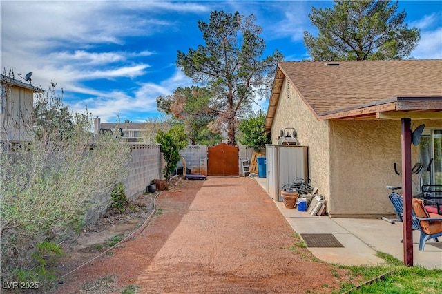 exterior space featuring stucco siding, a shingled roof, a gate, a patio area, and fence