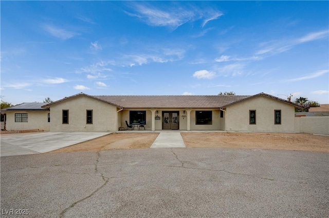 ranch-style home with french doors, fence, a tiled roof, and stucco siding