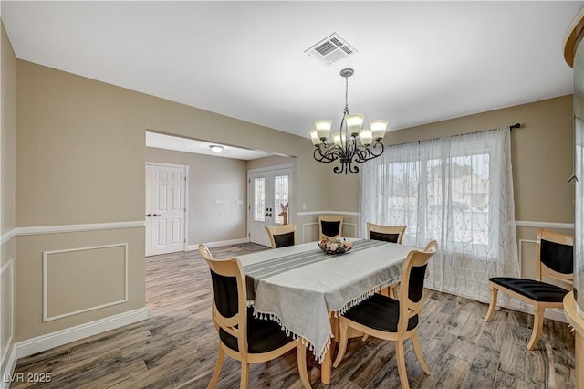 dining space with a notable chandelier, visible vents, wood finished floors, and french doors